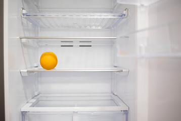 An orange lying against the background of a white empty clean refrigerator on a glass shelf. Clean fresh fridge after cleaning service or housewife