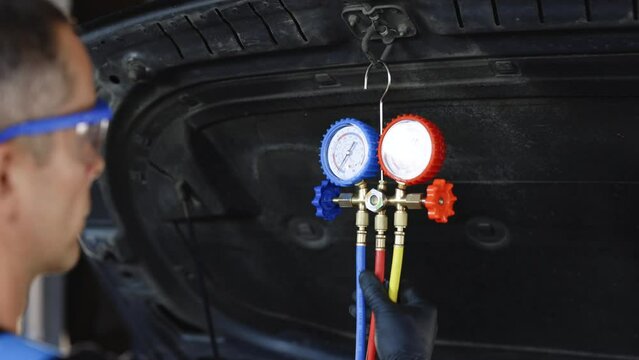 Car lies system of manometers for refueling air conditioner. Car refilling air condition in air shop. The hands of the master unscrew the protective cap of the air conditioner
