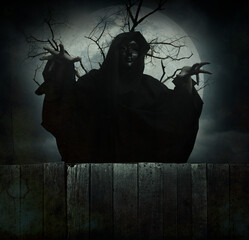 Grim reaper standing over dead tree, full moon and cloudy spooky sky, Halloween mystery concept
