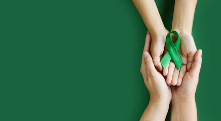 Adult and child hands holds green ribbon on green background. World lymphoma awareness day. September 15. Liver, Gallbladders bile duct, kidney Cancer and Lymphoma Awareness month.