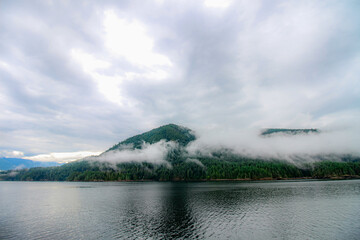 Journey on ferry from Sunshine Coast to Powell River. The view on the mountain in the distance surrounded by mist. Cloudy sky.