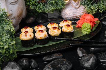 Served warm sushi rolled in nori sheets with ginger and wasabi on a black stone plate