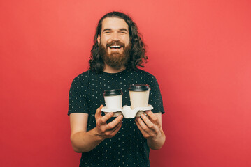 A photo of a delivery man holding two cup of coffee while smiling at the camera