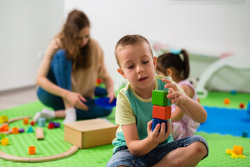 caucasian boy playing with wooden cubes toy in daycare - obrazy, fototapety, plakaty