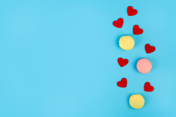 Tasty french macarons with red hearts on a blue pastel background. Pink and yellow macarons. Place for text..
