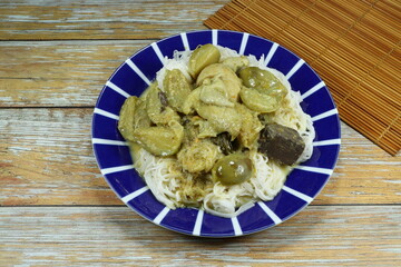 Traditional spicy green curry soup dressing on riced noodle serving on the plate. Famous steed food menu in Thailand.