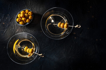 Martini, two glasses with spicy olives. Alcoholic cold drinks, shot from above on a black background with copy space, a flat lay - obrazy, fototapety, plakaty
