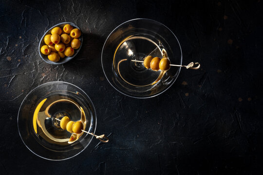 Martini, Two Glasses With Spicy Olives. Alcoholic Cold Drinks, Shot From Above On A Black Background With Copy Space, A Flat Lay