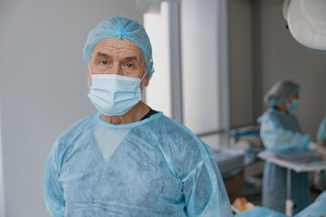 Close up of senior surgeon in mask standing in operating room, ready to work on patient