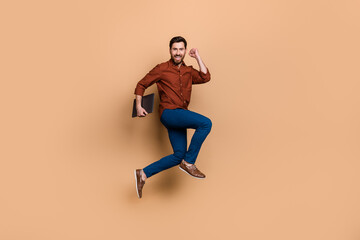 Fototapeta na wymiar Full length photo of delighted astonished person jumping raise fist celebrate achievement isolated on beige color background