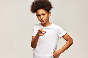 Frowning black teen boy in white mockup t-shirt with afro hairstyle posing on gray background with...