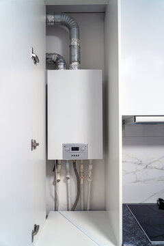 Opened Kitchen Cabinet And LPG Gas Boiler Inside Furniture. Gas Central Heating Condensing Boiler Fitted Inside Cabinet.