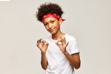 Cute smiling black boy kid with afro hairstyle and red bandana on head dressed in white t-shirt...
