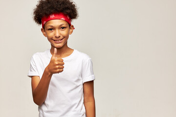 Portrait of happy satisfied boy kid with afro hairstyle in red bandana and white mockup shirt...