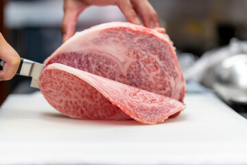 和食レストランの厨房で板前が丁寧に切り分ける、見事な霜降りの最高級和牛サーロインブロック肉の調理シーン。テキストを入れるスペースあり