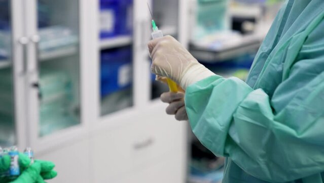 Medics in latex gloves taking medicines into syringe from a little bottle. Doctors at operation in modern surgery room. Blurred backdrop.
