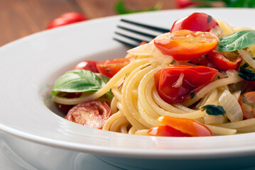 Piatto di deliziosi spaghetti con pomodori pachino, aglio, cipolla, basilico e olio extra vergine di oliva, cibo italiano - dieta mediterranea 