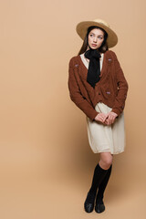 Full length of brunette woman in sun hat posing on beige background