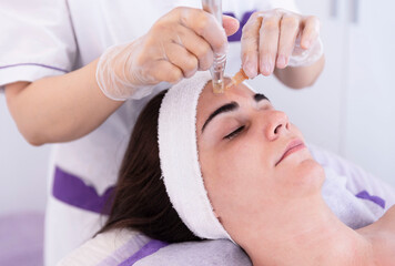close up of Cosmetologist,beautician applying facial dermapen treatment on face of young woman...