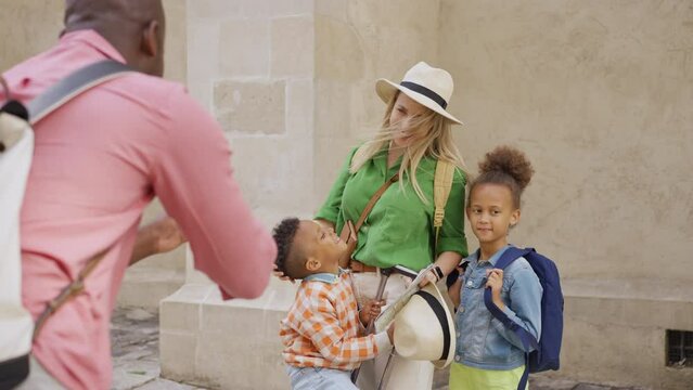 Multiracial family travelling together with small kids. Father taking photo of wife and kis in old city cetre.