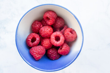 Red raspberry in a bowl on a white marble table background. Top view, flat lay, copy space. Healthy eating, cooking at home concept