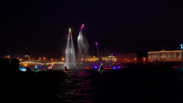 A lot of flyboarders and brightly dressed up jet skiers perform their show at a holiday in the center of St. Petersburg at night, water activities