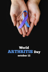 World Autoimmune Arthritis Day. Adult hands holding blue purple ribbon on black background. RA rheumatoid arthritis illness disease. Vertically Photo.