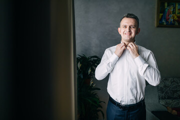 A man in a shirt. The groom in a white shirt, the groom fastens the shirt. The morning of the groom.