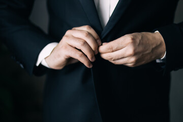 Obraz premium the groom's hands fasten his jacket in the morning before the wedding. close-up of a man in a black business suit
