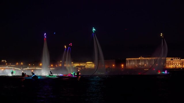 A lot of flyboarders and brightly dressed up jet skiers perform their show at a holiday in the center of St. Petersburg at night, water activities