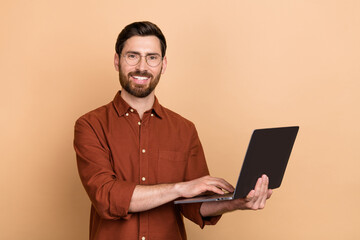 Photo of cheerful positive man toothy smile hold use wireless netbook isolated on beige color background