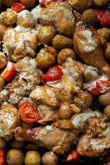 Baked chicken leg quarters seasoned with garlic and herbs with potatoes in a baking dish on a wooden table close up view