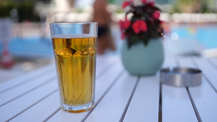 One cold alcoholic beer in transparent glass on sunny day by pool