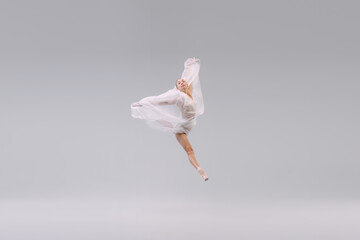 Portrait of young ballerina dancing, jumping with transparent fabric isolated over grey studio background. Leap
