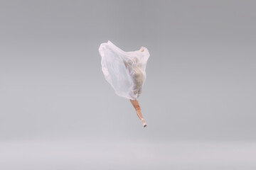 Portrait of young ballerina dancing, performing with transparent with fabric isolated over grey studio background. Weightlessness