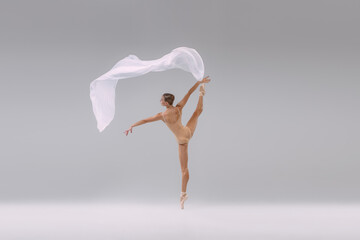 Portrait of young tender ballerina dancing in beige cloth with transparent fabric isolated over...