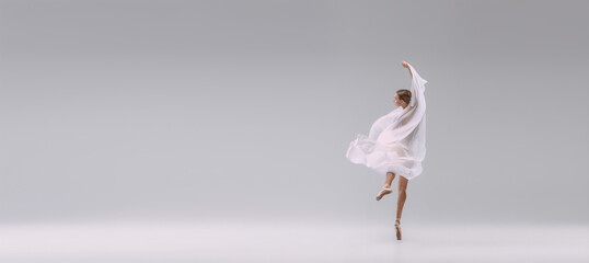Portrait of young ballerina dancing covered with white transparent fabric isolated over grey studio...