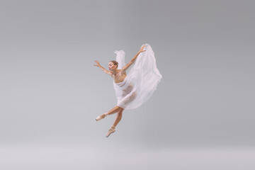 Portrait of young ballerina dancing with fabric isolated over grey studio background. The grace, artist, movement