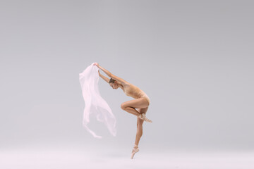 Portrait of young ballerina dancing with fabric isolated over grey studio background. Graceful,...
