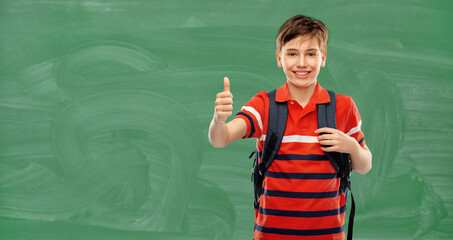 education, school and people concept - smiling student boy with backpack showing thumbs up over green chalkboard background