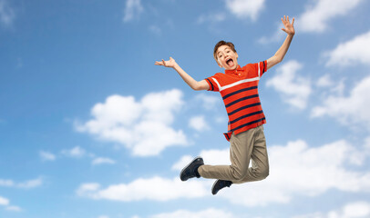 Fototapeta premium freedom, motion and happiness concept - happy smiling young boy jumping in air over blue sky and clouds background