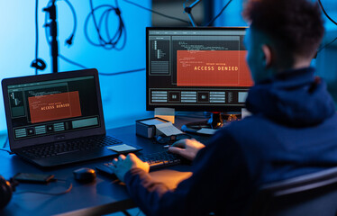 cybercrime, hacking and technology concept - male hacker in dark room writing code or using...