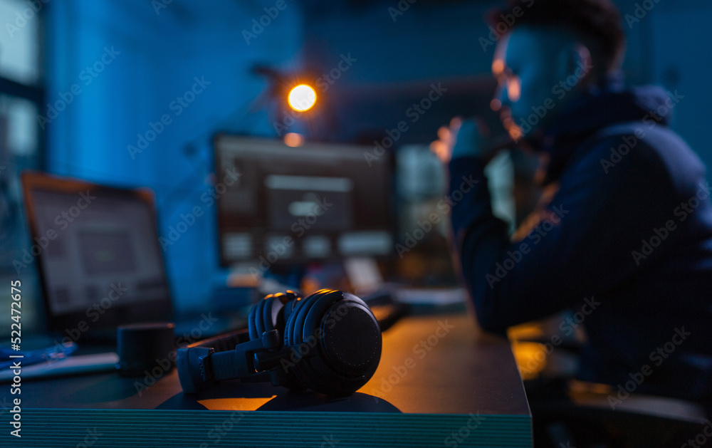 Poster cybercrime, hacking and technology concept - close up of male hacker in dark room with headphones us