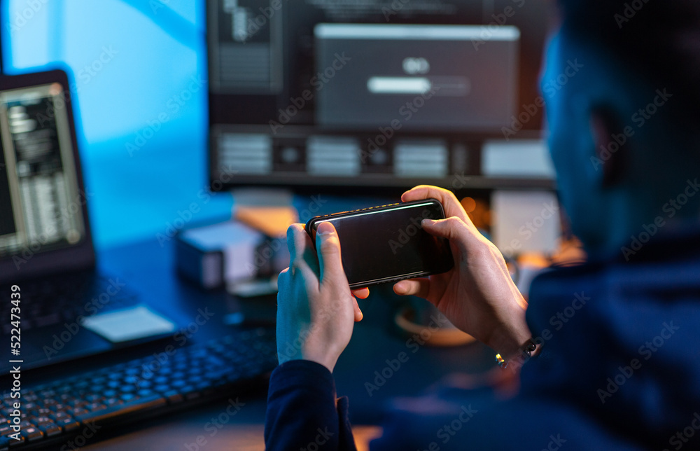 Poster cybercrime, hacking and technology concept - close up of male hacker with smartphone using computer 