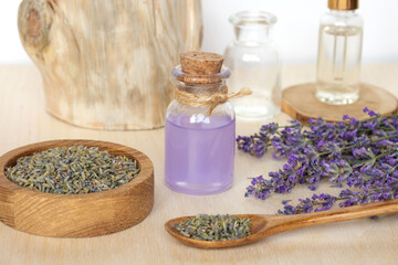 Obraz na płótnie Canvas Dry lavender flowers in wooden bowl and bottle of essential lavender oil or infused water on white background. Natural organic ingredients for herbal cosmetics. Spa massage set, lavender product