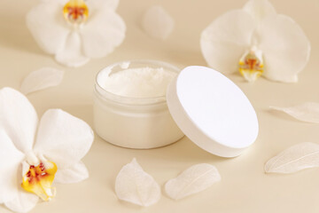 Fototapeta na wymiar Opened Cream jar with a blank lid near orchid flowers on light yellow close up. Cosmetic Mockup