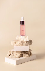 Pink glass cosmetic dropper bottle on beige travertine stones on light yellow close up