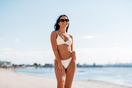 people, summer and swimwear concept - happy smiling young woman in bikini swimsuit on beach