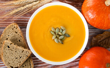 Delicate pumpkin cream soup with rye bread on a wooden table. Healthy food from seasonal vegetables. Top view. Close-up.