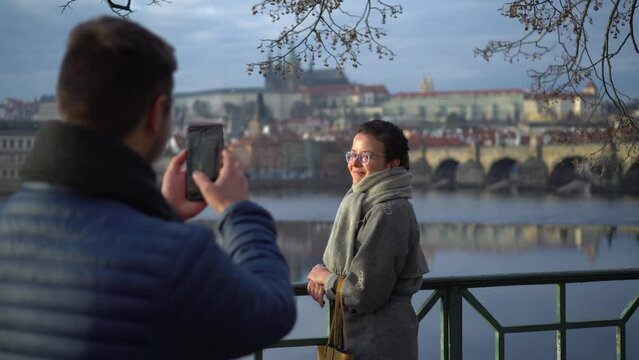 Man taking photo of his girl on mobile phone, Prague Castle and Charles Bridge in background, Czech Republic